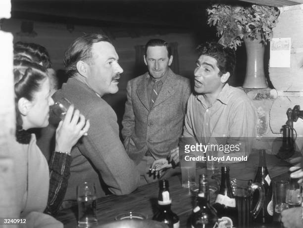 Hungarian-born photojournalist Robert Capa talks to American writer Ernest Hemingway while standing at a bar at Trail Creek Cabin, Ketchum, Idaho....