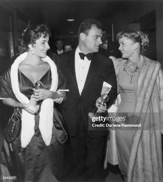 From left to right, British-born actor Elizabeth Taylor and her husband, film producer Mike Todd , hold their Golden Globe awards while walking with...