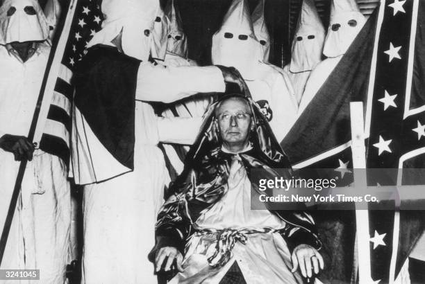Hooded Klansmen holding American and Confederate flags surround Lycurgus Spinks as he is crowned imperial emperor of the Ku Klux Klan during a...