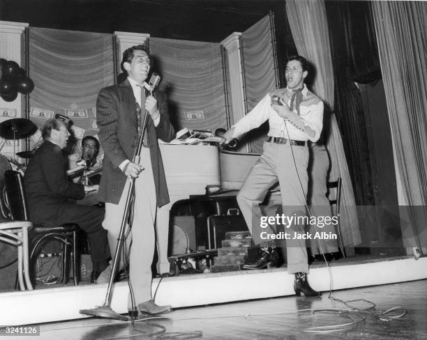 American comic team Jerry Lewis and Dean Martin sing into microphones onstage while performing at a SHARE Boomtown party for charity. Behind them...