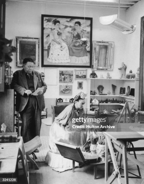 Married Mexican artists Diego Rivera and Frida Kahlo read and work in a studio. Kahlo's self-portrait, 'The Two Fridas' , hangs in the background...