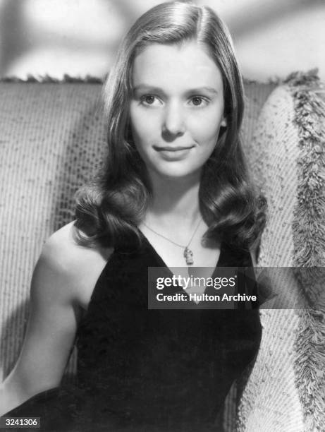 Portrait of American actor Susan Strasberg , wearing a black, sleeveless V-neck dress with an angel amulet. She sits against a fringed cushion.