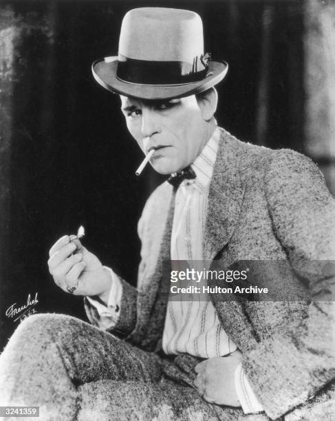 Promotional portrait of American actor Lon Chaney lighting a cigarette in his role for director Tod Browning's film, 'Outside the Law'. He wears a...