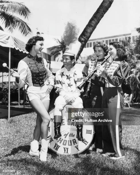 Full-length image of American jockey Willie Shoemaker sitting outdoors on a large drum, surrounded by three University of Miami Marching Band...