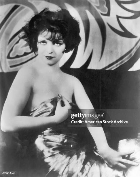 Portrait of American actor Clara Bow , bare shouldered, smiling while holding a lame sheet to her chest.