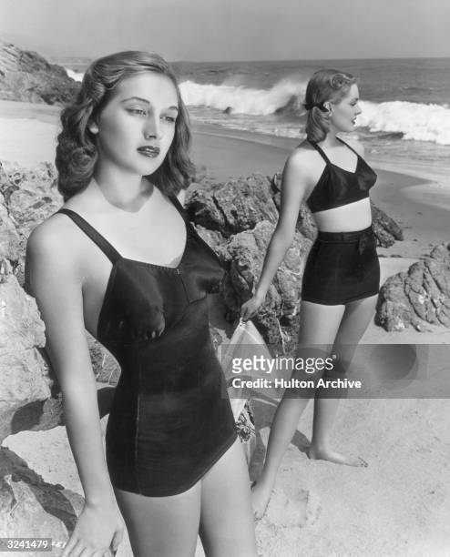 Model and actor Georgia Lange , one of the 'Goldwyn Girls,' wears a one-piece black satin latex bathing suit on a beach, as another woman in a...
