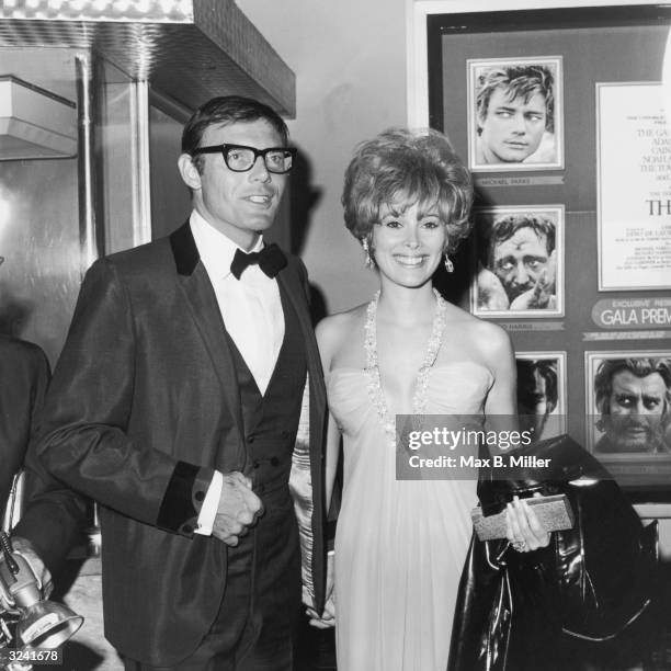 American actors Adam West and Jill St. John smile and hold hands at the premiere of director John Huston's film, 'The Bible.' They are standing in...