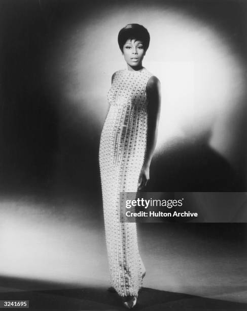 Full-length studio portrait of American actor Diahann Carroll wearing a long, gemstone-studded, sleeveless dress.