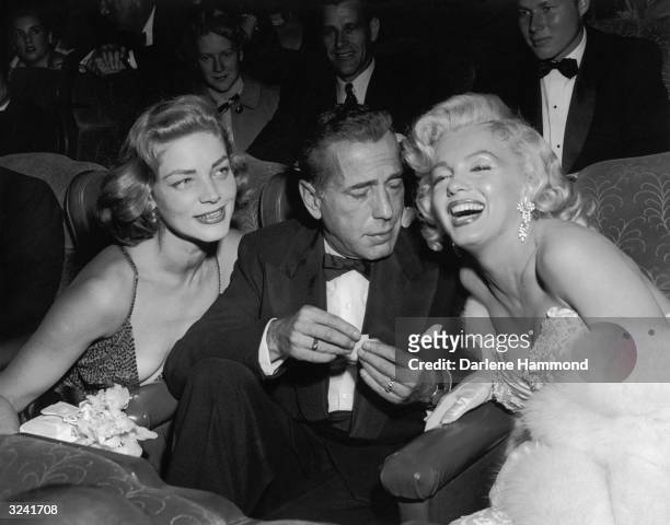 Married American actors Lauren Bacall and Humphrey Bogart pose with American actor Marilyn Monroe at the premiere of director Jean Negulesco's film,...