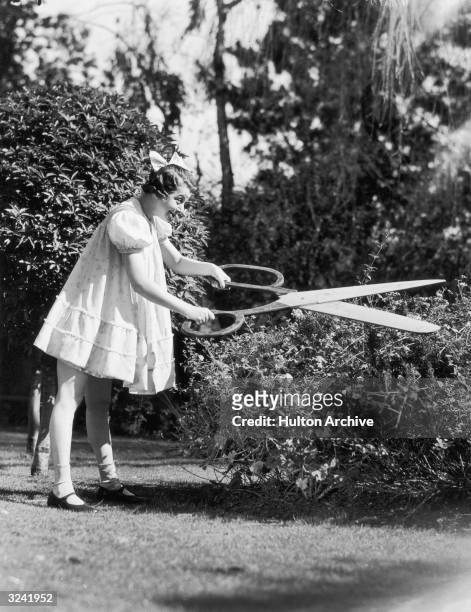 American actor and singer Fanny Brice as 'Baby Snooks,' trimming a rosebush with large pair of scissors.