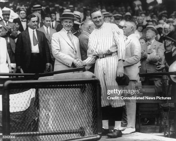 President Calvin Coolidge smiles and shakes hands with Washington Senators pitcher Walter Johnson at Griffith Stadium, as people look on in the...