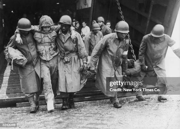 Wounded American soldiers are helped ashore by Black soldiers at a British port, after arriving from France during World War II. The soldiers had...