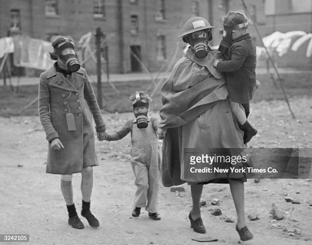 Woman with a girl and two young boys, all wearing gas masks, walk to an air raid shelter during a drill at Aldershot, England.