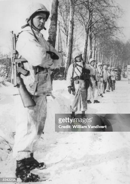 American soldiers wearing snow suits line the road to St Vith during the final liquidation of the German salient.