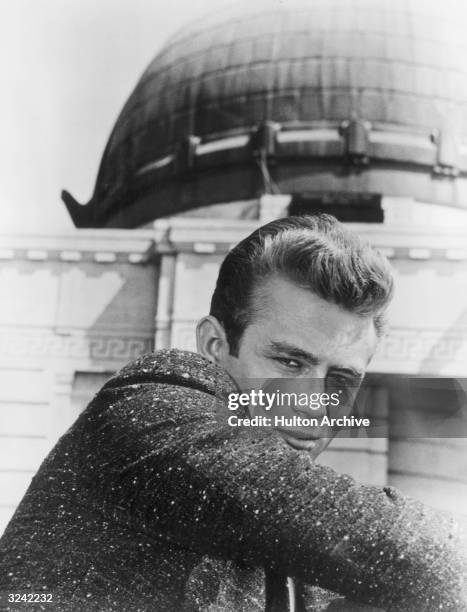 American actor James Dean , as Jim Stark, looks over his shoulder while sitting in front of the Griffith Observatory in a promotional portrait for...