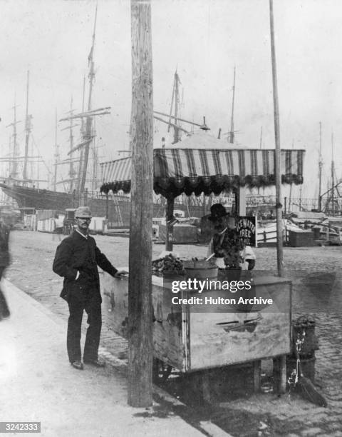 Customer buys a snack at a fresh oyster stand on South Street, near the harbor, New York City, 1880s.