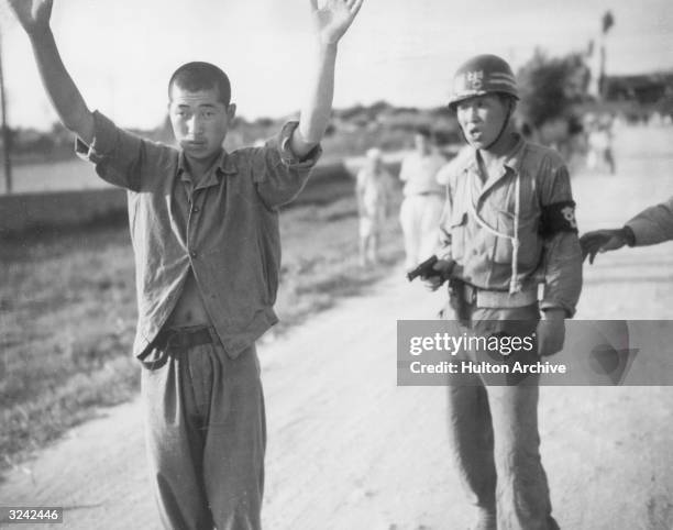 South Korean policeman holds a North Korean prisoner of war at gun point as he marches him to a stockade during the Korean War, Korea.