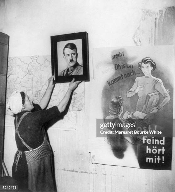 Woman removes a portrait of Hitler from the wall of a protestant church in Frankfurt, which had been used by the Nazis as a party headquarters. On...