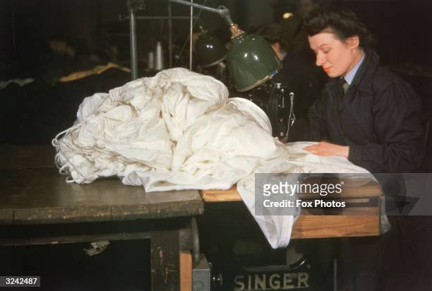 Woman uses a Singer sewing machine to stitch a bundle of parachute silk.