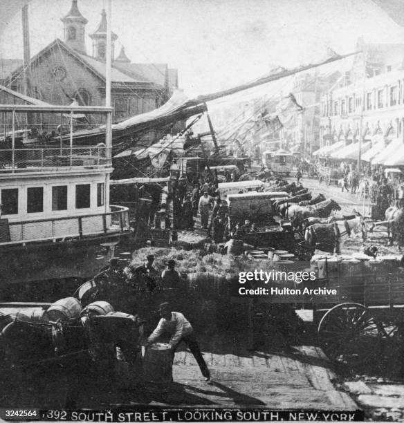 Workers unload barrels of merchandise from ships docked along South Street, New York City, 1880s.