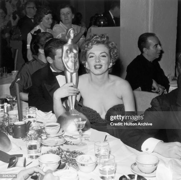 American actress Marilyn Monroe , in a low-cut strapless velvet dress, poses with her 'Henrietta' statuette at the Foreign Press Association of...