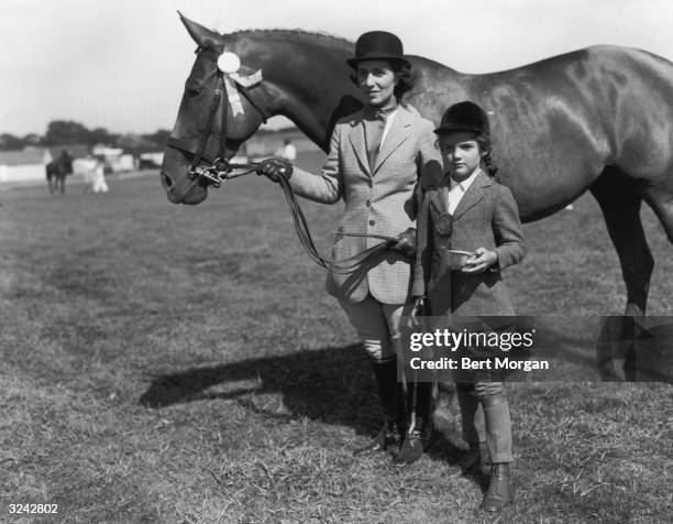 Full-length portrait of Jacqueline Bouvier holding a riding crop and small bowl while standing beside her mother, Mrs John V Bouvier III, who is...