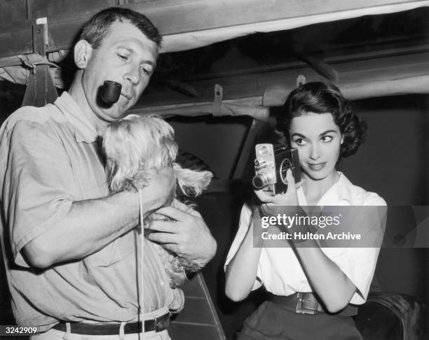 American director Richard Brooks smokes a pipe and holds actor Dana Wynters's small dog, a miniature Skye terrier, while Wynter points a handheld...