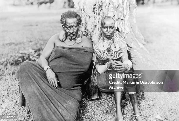 Meru chief, wearing a five pound stone in his earlobe, sits with his young wife under a tree, Africa. Photographed by the husband and wife explorers...