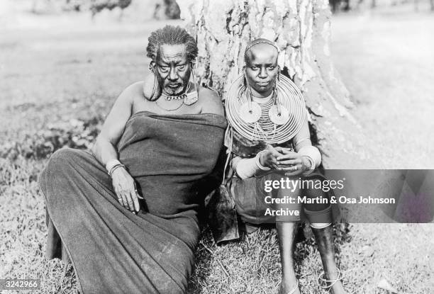 Meru chief, wearing a five pound stone in his earlobe, sits with his young wife under a tree, Africa. Photographed by the husband and wife explorers...