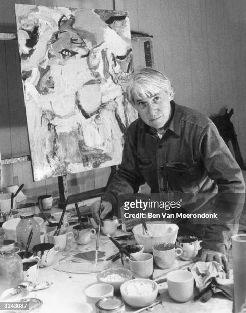 Dutch-born painter Willem de Kooning looks at the camera as he mixes paint on a large workbench, painting a canvas in his studio in Easthampton, Long...