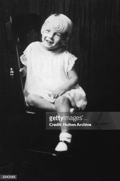 Portrait of American actor Marilyn Monroe at age 5, sitting in a wooden chair.