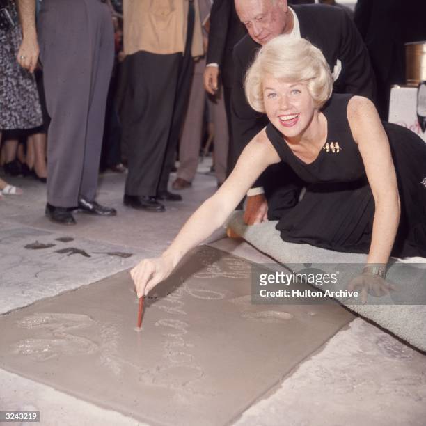 American singer and actress Doris Day smiling as she signs her name in cement by her handprints, in front of Mann's Chinese Theater, on Hollywood...
