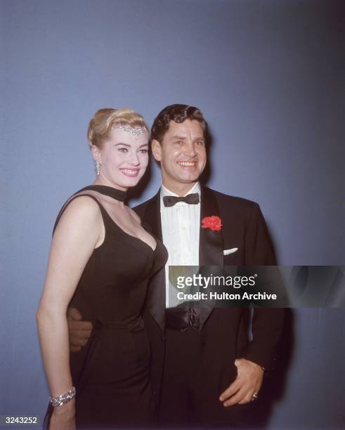 Swedish actor Anita Ekberg, wearing a black dress and a diamond jewelry on her head, poses with her husband, British actor Anthony Steel, who wears a...
