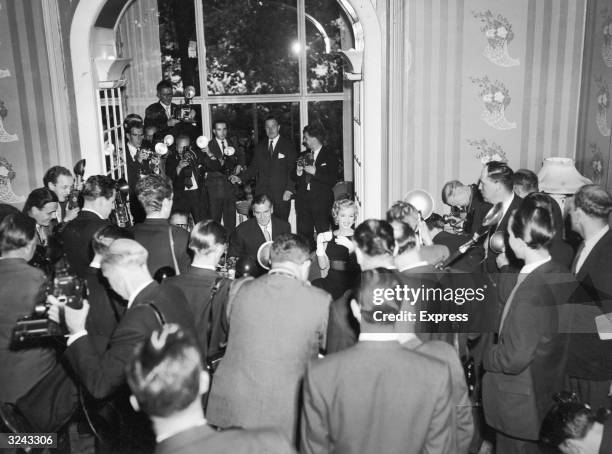 American actor Marilyn Monroe, drinking tea, and English actor Sir Laurence Olivier are surrounded by photographers during a press conference at the...