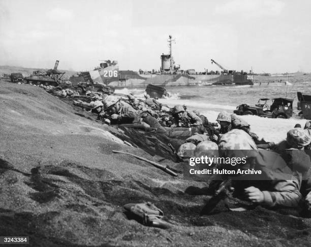 United States Fourth Division Marines take cover from enemy fire on the shores of Iwo Jima during World War II, Japan. A US battleship and amphibious...