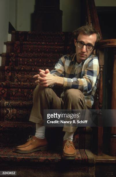 Portrait of American actor and film director Woody Allen sitting on a stairwell and leaning against a banister, with his hands clasped over one knee.