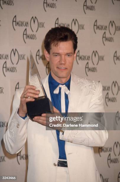 American country singer Randy Travis smiles as he holds his award at the American Music Awards, Los Angeles, California. Travis is wearing a white...