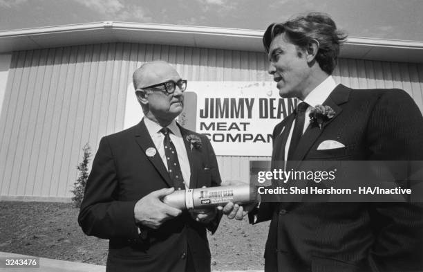 American country singer and business executive Jimmy Dean and an elderly man hold a tube of sausage at the opening of a new Jimmy Dean Meat Company...