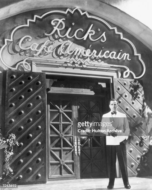 American actor Humphrey Bogart smokes a cigarette outside Rick's Cafe Americain in a publicity still from director Michael Curtiz's film,...
