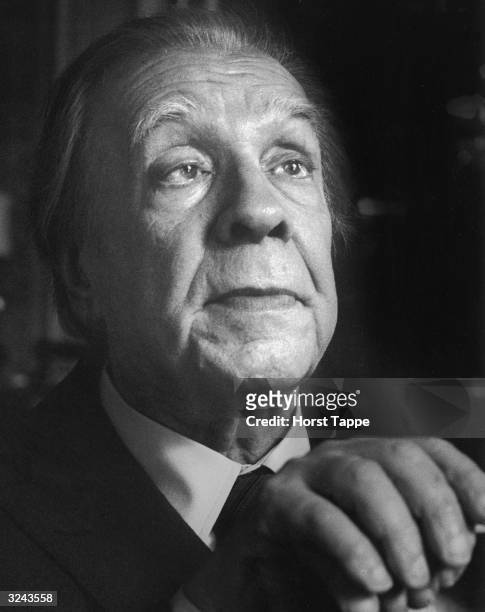 Headshot of Argentine author Jorge Luis Borges looking up with his hands folded in front of his chin.