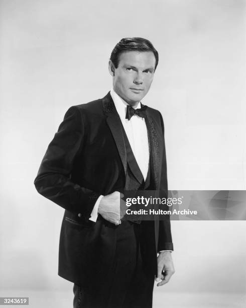 Promotional studio portrait of American actor Adam West, from the television series 'Batman' standing with his thumb in the vest pocket of his tuxedo.