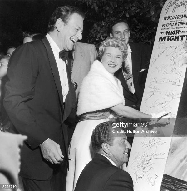 American actors John Wayne , Claire Trevor with American actor and singer, Phil Harris signing a tablet at the premiere of director William A...