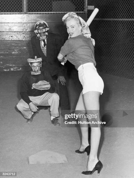 American actor Marilyn Monroe , wearing shorts and high heels, prepares to swing a baseball bat during a 20th Century Fox Studio baseball league...