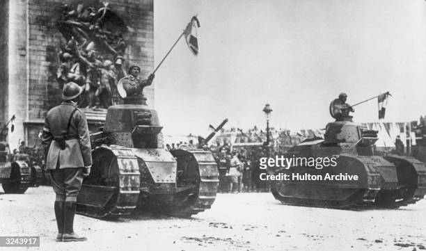 French soldiers holding flags and riding in tanks in front of the Arc de Triomphe on the Champs Elysees during a Bastille Day Victory Parade...