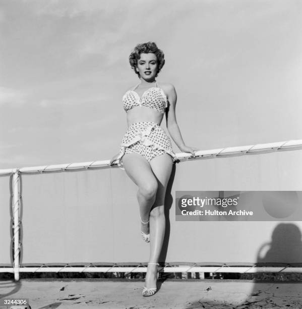 Full-length portrait of American actor Marilyn Monroe standing in a two-piece polka dot bathing suit and heels.
