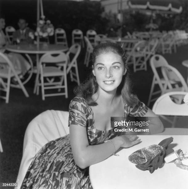 Italian actor Pier Angeli sits at a patio table wearing a floral print dress at a Louella Parsons' party, Los Angeles, California, mid 1950s.