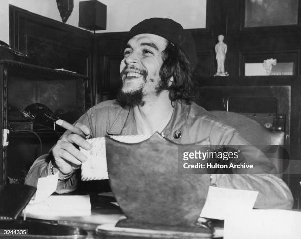 Argentinian-born revolutionary Ernesto 'Che' Guevara , Cuban minister of industry, sits at a desk and smokes a cigar.
