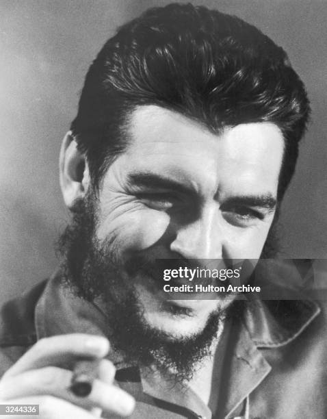 Closeup of Ernesto 'Che' Guevara Cuban minister of finance, smoking a cigar in military fatigues.