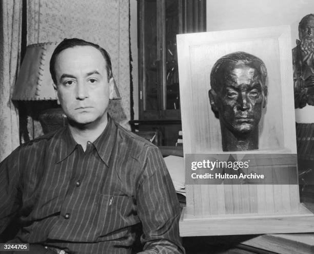 Portrait of Romanian-born director Jean Negulesco sitting beside a stone bust of his head.