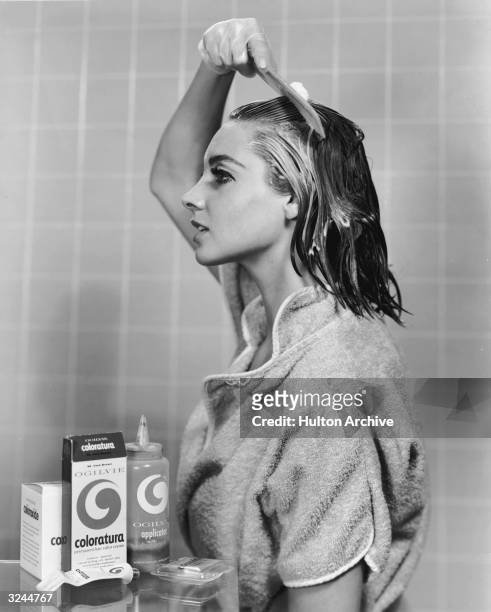 Woman in a terry cloth robe uses a comb to apply dye from a Coloratura home hair coloring kit in a bathroom.